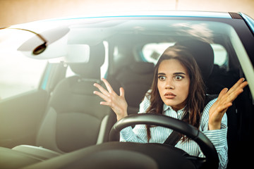 Closeup portrait, angry young sitting woman pissed off by drivers in front of her and gesturing with hands. Road rage traffic jam concept. 