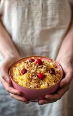 Pink plate of corn porridge with granola and berries in the hands of a girl. Healthy diet, vegan or food concept for social media.
