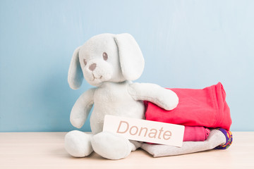 light blue plush puppy and a stack of children's clothing for a donation, blue background, copy space, Jonate inscription on cardboard