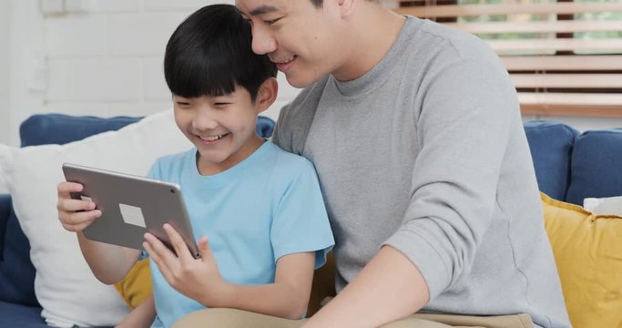 Little boy and father using tablet together with smile. They using tablet to find knowledge or playing game together at home. Technology, Lifestyle, Family and Education concept.