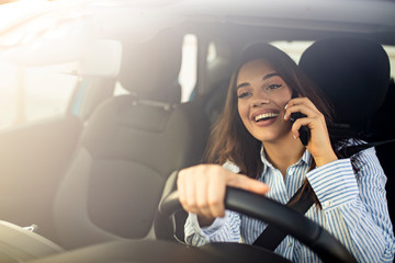 Young beautiful woman in a car talk on the phone and driving - multitasking lady drives with...