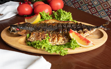 grilled fish with vegetables on a wooden plate and slices of lemon