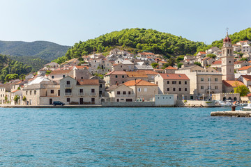Fototapeta na wymiar Pucisca town at Brac in Croatia, view from the sea on a sunny day in the summer. The port with it’s famous limestone from the island. Small idyllic place, village in Dalmatia. Holiday destination