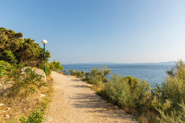 Fototapeta na wymiar Makarska in Dalmatia, Croatia. View from the peninsula on a sunny day in summer with a blue sky. Rough nature, a path with greenery, trees and rocks and the Adriatic sea at the Mediterranean coast
