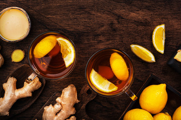 Healing black herbal tea with ginger, honey, lemon. Immune booster drink in glass cup on rustic wooden background with copy space. Top view