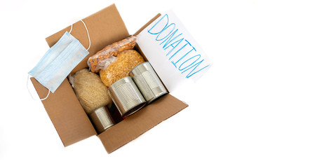 Coronavirus donation concept. Donation box with food isolated on white. Canned food, dried peas, rice, nuts. Top view. Copy space