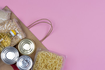 Paper bag with a crisis food supply for the period of quarantine isolation on a pink background with a copy of space, pasta, oatmeal, canned food. The food delivery, a donation during a pandemic