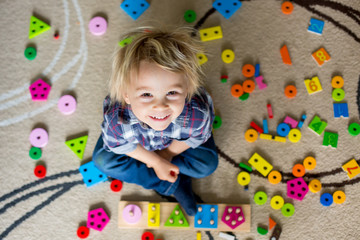 Little blonde toddler child,  boy playing with wooden toys developing and learning