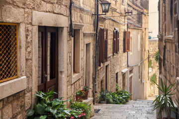 Korcula old narrow Mediterranean street with stairs. Rough stone houses, facades with windows, green plants, flowers in Dalmatia, Croatia. Historical place creating a picturesque and idyllic scenery