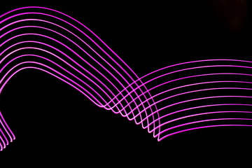 Long exposure photograph of neon pink colour in an abstract swirl, parallel lines pattern against a black background. Light painting photography.