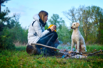 Woman with a dog near a bonfire on a picnic.
