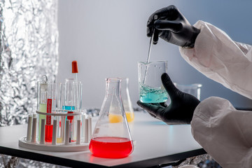 A close-up portrait of a chemist wearing protective gloves, holding a flask of red  liquid....