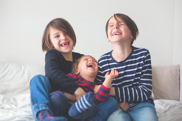 Three children, boy brothers, laughing in bed