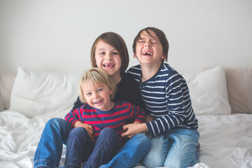 Three children, boy brothers, laughing in bed