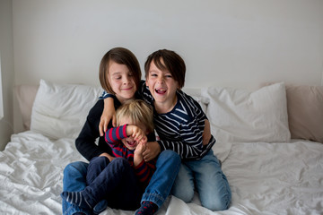 Three children, boy brothers, laughing in bed