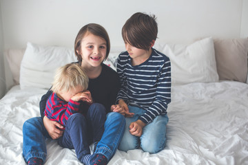 Three children, boy brothers, laughing in bed
