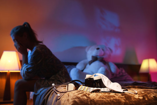 Focus photos: medicines, mask and stethoscope. On blurred background: Depressed woman wakes up at night, she is exhausted and suffers from high body temperature. Epidemic. Influenza, pneumonia, virus