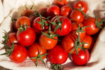 Small round cherry tomatoes with cuttings on a white napkin, wooden background. Delicious healthy vegetables, raw food.