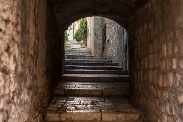Fototapeta na wymiar Old Mediterranean street with an arch stairs in Korcula. Rough stone houses and facades and green plants in Dalmatia, Croatia. Historical place creating a picturesque and idyllic mindful scenery