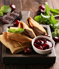 Russian cuisine. Pancakes with chocolate filling and cherry jam, fresh mint on a wooden board on an...