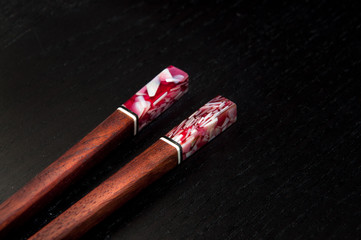 Wooden chopsticks with colorful stone detail on the top. Dark background. close up