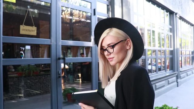 blonde woman in black glasses and hat near the entrance to the restaurant