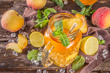 Fototapeta na wymiar Fresh Homemade Peach Sweet Tea with Mint and Lemon Slices, Summer cold fruit drink. Wooden background with fresh peach, copy space