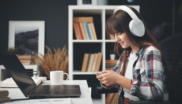 Side view of female teenager using digital gadgets sitting at table while studying at home