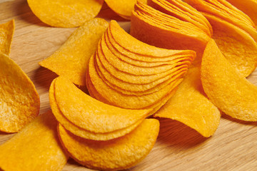 A bunch of potato chips on the wooden background. Appetizing orange flavored snacks. Closeup.