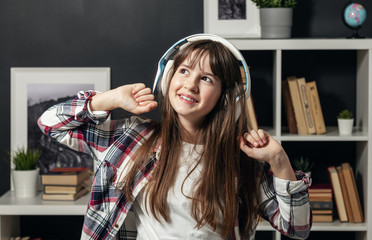 Waist-up shot of teen girl looking aside and stretching while listening to music or audio lesson, front view