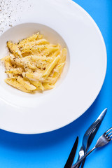 Tasty appetizing classic italian penne pasta with creamy sauce and cheese parmesan on plate on blue table. View from above.