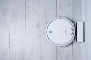 White robotic vacuum cleaner charging on white wooden floor in the living room. Smart electronic housekeeping technology
