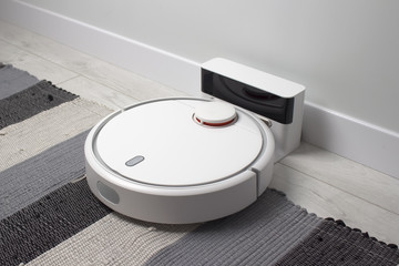 White robotic vacuum cleaner charging on white and black carpet in the living room. Smart...