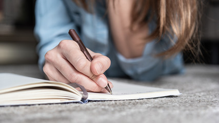 Close up woman hand writing in diary, lying on the floor.