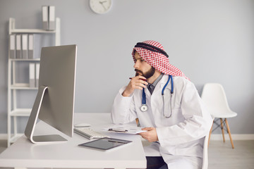 Arab male doctor working at a table with a computer in the office of a medical clinic.