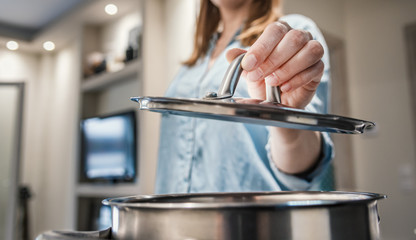 Close up woman hand lifting a saucepan lid.
