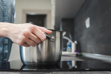 Putting saucepan with water on induction cooktop.