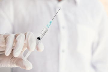 Hand in surgical gloves holding medical injection syringe. Selective focus, copy space