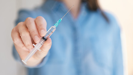 Woman holding medical injection syringe in her outstretched hand extended towards the camera