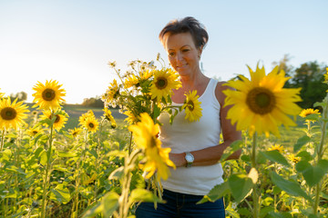 Happy mature beautiful woman holding flowers while thinking in the sunflower garden farm