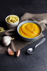 Butternut squash soup with croutons and fresh garlic in ceramic bowl with spoon on grunge black background with linen napkin