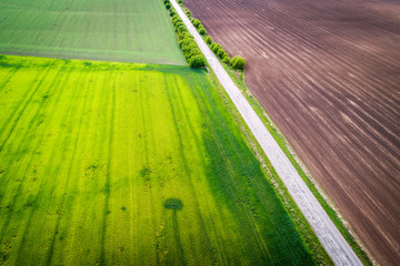 Aerial view of agricultural fields and broken patched road. Natural grass.