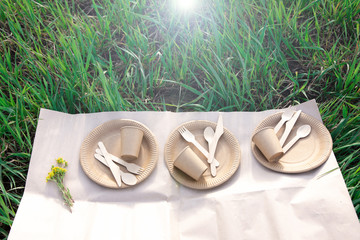 Three sets of disposable wooden forks, spoons, knives and paper cups and plates on craft paper on...