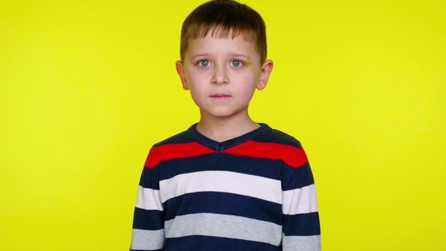 Serious little child boy in a colorful sweater says yes on a yellow background with copy space. Place for text or product. 4K slowmotion footage