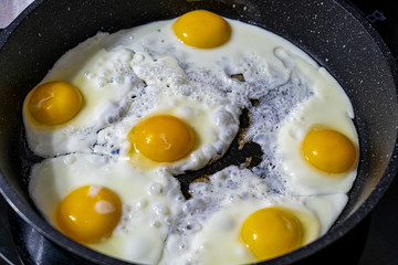 Closeup view of fried eggs which are being cooked on black frying pan in the morning at kitchen