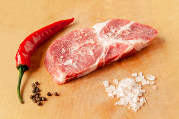 A piece of steak lies on a cutting board, next to salt, pepper.