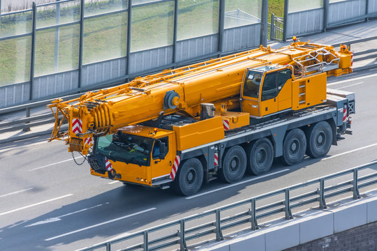 Heavy mobile crane with folding boom construction rides on a city highway.