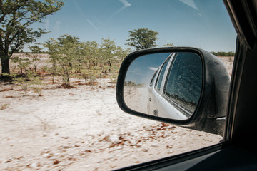 View in rear view mirror while driving through arid dry landscape in Etosha national park Namibia.