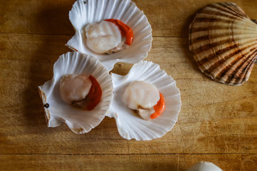 raw scallops and shells on a wooden cutting board close up