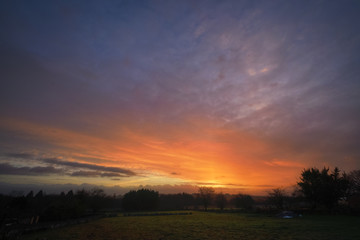 Fototapeta na wymiar Orange fiery Cloudscape at Sunrise over Pasture land